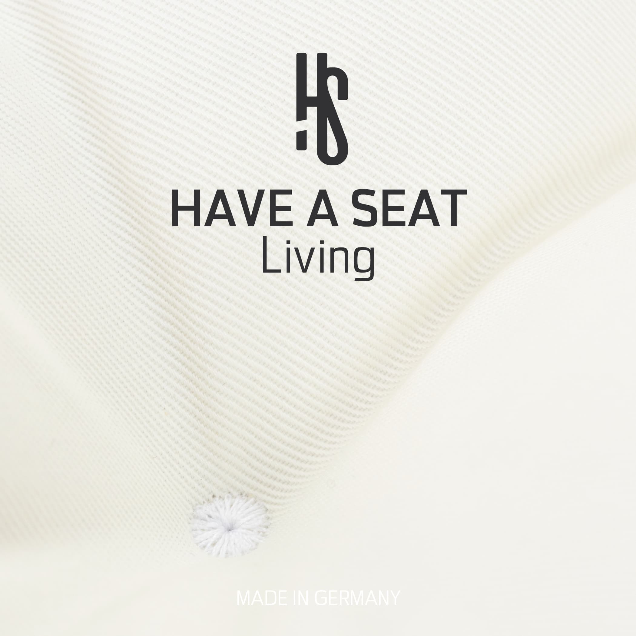 Nahaufnahme des Weissen Stoffbezugs mit Markenlogo „Have A Seat Living“ und Hinweis „Made in Germany“.