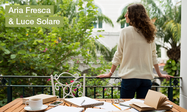 Aria fresca e luce solare &ndash; donna sul balcone con vista sul verde, quaderno e caff&egrave; sul tavolo