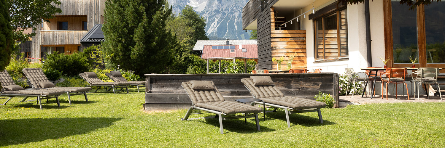 Mehrere Sonnenliegen im Garten eines Wellnesshotels mit strapazierfähigen HAVE A SEAT Living Premium-Liegenauflagen und Nackenkissen, waschbar & UV-beständig, für Hotellerie & Spa