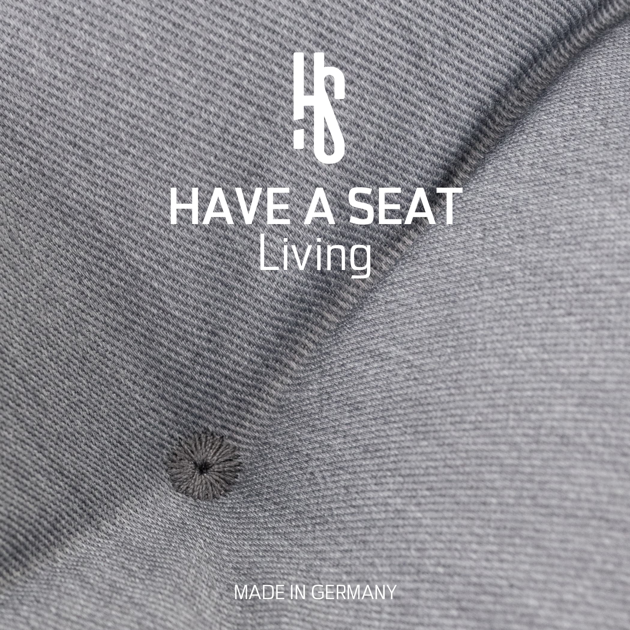 Nahaufnahme des Hellgrauen Stoffbezugs mit Markenlogo „Have A Seat Living“ und Hinweis „Made in Germany“.